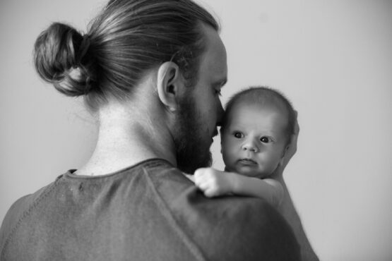 Closeup portrait of young bearded Caucasian father hugging and kissing newborn baby. Male man parent holding child. Authentic lifestyle touching tender moment. Single dad family life concept.Studio portrait of a happy father with a baby in his arms